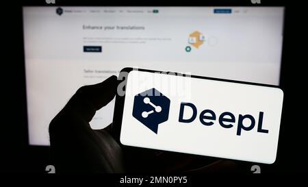 Person, die ein Handy mit dem Logo des neuronalen maschinellen Übersetzers DeepL auf dem Bildschirm vor der Webseite hält. Konzentrieren Sie sich auf das Display des Telefons. Stockfoto