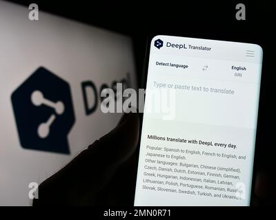 Person mit Handy und Website des neuronalen maschinellen Übersetzers DeepL auf dem Bildschirm vor dem Logo. Konzentrieren Sie sich auf die Mitte des Telefondisplays. Stockfoto