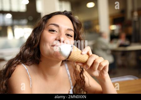 Eine glückliche Frau, die Eiscreme isst, sieht dich in einem Café an Stockfoto