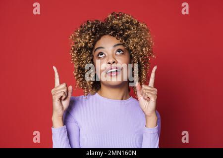 Junge, wunderschöne, attraktive, geschwungene Frau, die auf einen isolierten roten Hintergrund zeigt Stockfoto