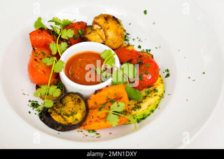 Essen in einem Restaurant auf einem weißen Teller. Ein Mann isst mit einer Gabel gegrilltes Gemüse, Auberginen, Karachok, Zucchini, Pilze, Champignons, Pfeffer und rote Soße. Hochwertige FullHD-Aufnahmen Stockfoto