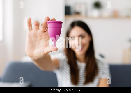 Lächelnde junge Frau mit wiederverwendbarer Menstruationstasse aus Silikon. Konzentrieren Sie sich auf den Vordergrund Stockfoto