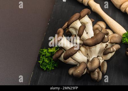 Köstliche Austernpilze aus biologischem Anbau mit Gewürzen und frischer Petersilie auf Holzbrett. Quelle des Beta-Glukans, schwarzer Steinbetonhintergrund, oben Stockfoto
