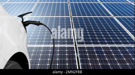 Nahaufnahme eines Elektroautos mit angeschlossenem Ladekabel auf dem Hintergrund von Solarmodulen Stockfoto