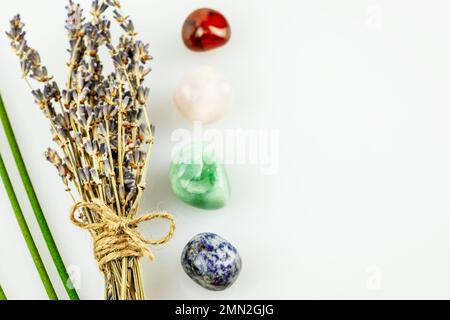 Erholende, energiereifende Zusammensetzung mit Lavendelblumen, Aromasticks und Chakrasteinen auf weißem Hintergrund mit Kopierbereich. Konzept der Entspannung, Stockfoto