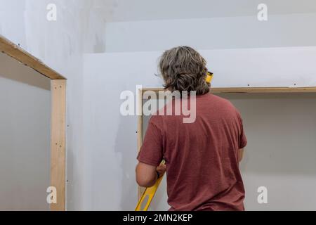 Arbeiter, die eine Hilfsstufe verwenden, prüfen den Füllstand von Trockenbauwänden vor dem Lackieren, um sicherzustellen, dass er gleich ist Stockfoto