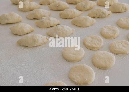 Zubereitung von mit Füllung gefüllten Brötchen und Donuts aus Hefeteig auf einer weißen Arbeitsfläche Stockfoto