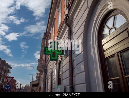 Fossano, Italien - 28. Januar 2023: Leuchtendes grünes Apotheke-Schild auf altem italienischen Gebäude. Tex: Farmacia (Apotheke) Stockfoto