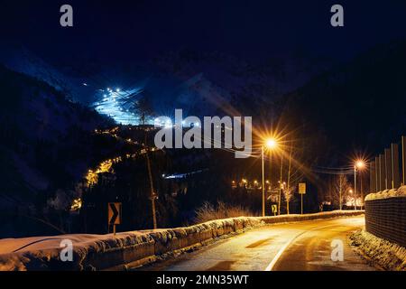 Landschaft der glühenden Straße von Medeu Schlittschuhlaufen zum Shymbulak Skigebiet in den Tian Shan Bergen bei Nacht in Almaty City, Kasachstan Stockfoto