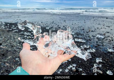 Nahaufnahme einer Touristenfrau, die im Sommer Gletschereis auf dem Island Place namens Diamond Beach hält. Stockfoto