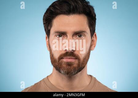 Porträt eines gutaussehenden bärtigen Mannes, der posiert und in die Kamera schaut, über blauem Studiohintergrund steht, Nahaufnahme eines Porträts Stockfoto
