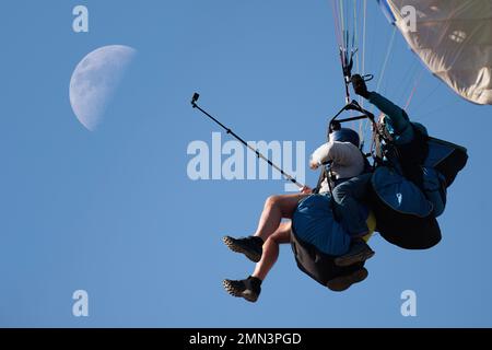 Paraglider-Tandem fliegen gegen den blauen Himmel, Tandem-Gleitschirmfliegen geführt von einem Piloten im Hintergrund mit dem Mond Stockfoto