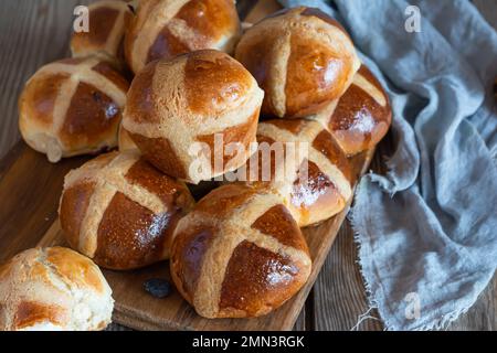 Heiße Brötchen mit Rosinen, traditionelles englisches (europäisches) Gebäck zu Ostern auf einem Holzbrett. Köstliches süßes Gebäck. Stockfoto