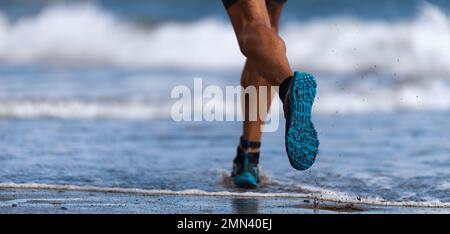 Sportler, der auf Wellen am Strand läuft Stockfoto