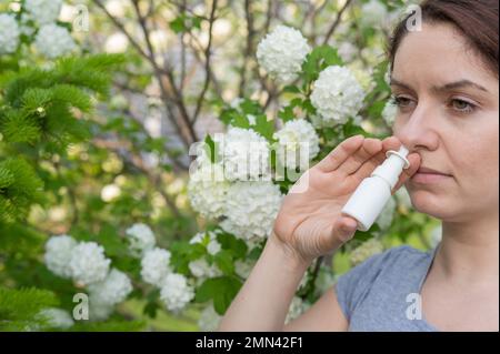 Kaukasische Frau verwendet ein Nasenspray, während sie im Park spazieren geht. Stockfoto