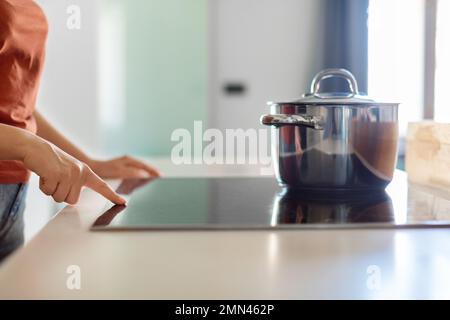 Weibliche Hand, die Induktionsherd mit Stahlpfanne in der Küche anmacht Stockfoto