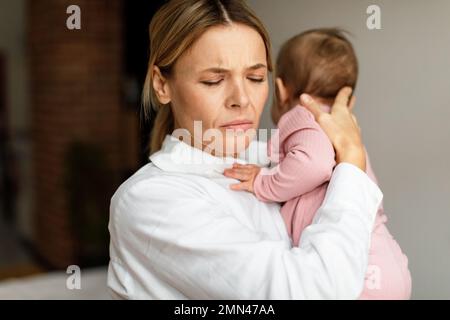 Erschöpfte Mutter, die ein kleines Baby hält, im Schlafzimmer zu Hause steht, Kopierraum Stockfoto