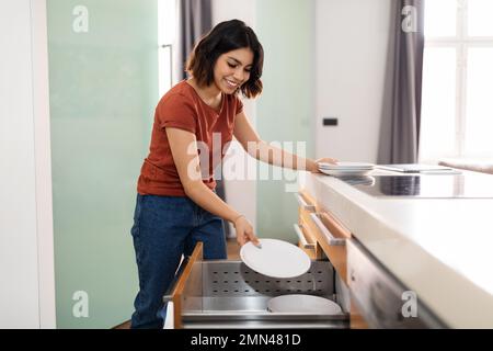 Wunderschöne junge araberin, die während der allgemeinen Reinigung den Küchenschrank aufräumt Stockfoto