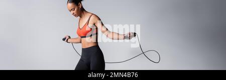 Sportliche afroamerikanische Frau, die mit einem Seil auf grauem Hintergrund trainiert, Banner Stockfoto