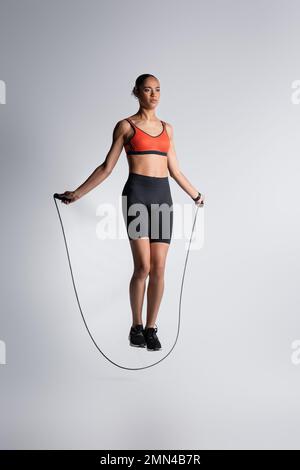 Die gesamte Länge einer afroamerikanischen Sportlerin, die mit einem Seil auf Grau trainiert Stockfoto