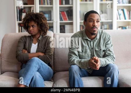 Trauriger schwarzer Mann und traurige Frau, die zu Hause auf der Couch sitzen Stockfoto