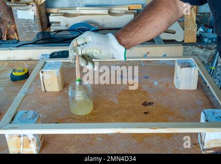 Fokussierter Hobbybastler aus dem mittleren Erwachsenenalter lackiert ein Holzbrett mit Schutzöl Stockfoto