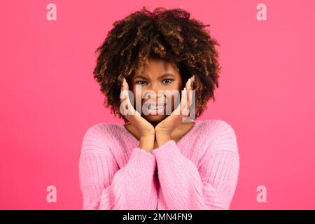 Traurige, unzufriedene, lächelnde junge, schwarze, geschweifte Dame mit einer Zahnspange in lässiger Form presst Hände auf die Wangen und leidet an Zahnschmerzen Stockfoto