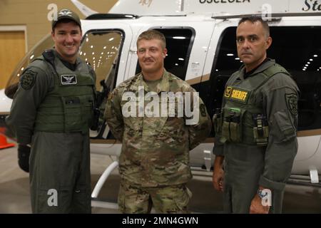 Stephen Kersey, Pilot beim Osceola Sheriff’s Department (links), SPC. Hunter Wolfe, ein Air Dense Battle Management Systems Operator mit der 1-265. Air Defense Artillery (Middle), und Sergeant Brian Demeulenarere vom Osceola County Sheriff’s Department posieren für ein Foto vor dem Hubschrauber, der als Reaktion auf den Orkane Ian verwendet wird. Der Hubschrauber und sein Pilot Stephen Kersey warten in einem Unterschlupf bei der Florida National Guard in Kissimmee, Florida, USA, 28. September 2022. Stockfoto