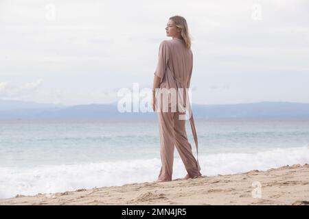 Porträt einer wunderschönen jungen Frau in beigefarbenem Seidenkostüm am leeren Sandstrand, idyllischer Sommerurlaub weit weg von der Stadt Stockfoto