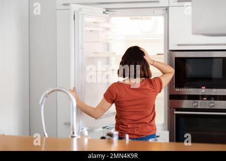 Junge Frau, Die In Einen Leeren Kühlschrank Schaut, Ohne Essen, Rückansicht Stockfoto