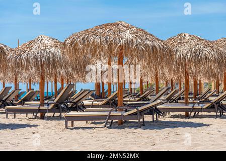 Strohschirme und Sonnenliegen am Meer. Stockfoto