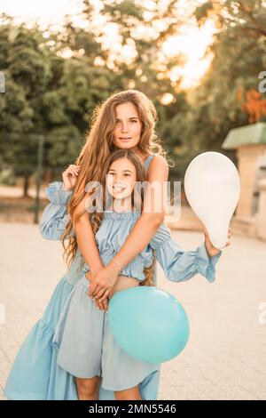 Mutter-Tochter-Sonnenuntergang. In blauen Kleidern mit fließenden langen Haaren Stockfoto