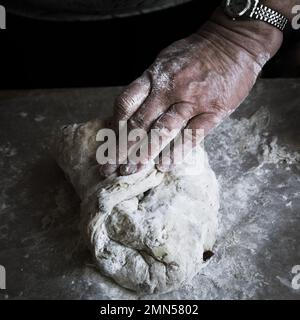 Großmutters Hände kneten Brotteig auf einer mehlvollen Oberfläche Stockfoto