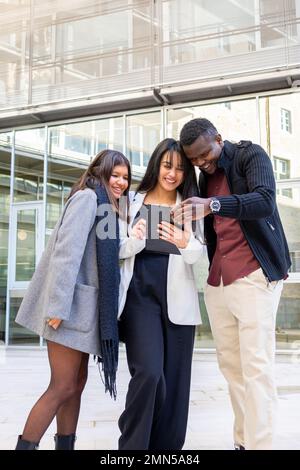 Attraktive Kollegen, die ein Tablet außerhalb des Büros verwenden. Gruppe junger Freunde, die bei der Arbeit in der Stadt lächeln. Ethnische Vielfalt, soziale Eingliederung Stockfoto