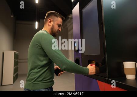 Ein weißer Mann gießt sich Kaffee aus einem Automaten ein. Stockfoto