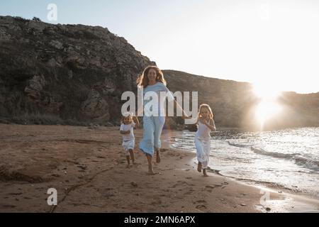 Mutterliebe. Mama umarmt ihre Töchter, küsst und spielt, zärtlich und fürsorglich. Freundliche Familie zu Hause und im Urlaub. Stockfoto