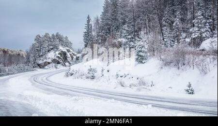 Glatte Landstraße im verschneiten Wald im Winter. Keine Autos. Schlechte Fahrbedingungen. Skandinavien. Stockfoto