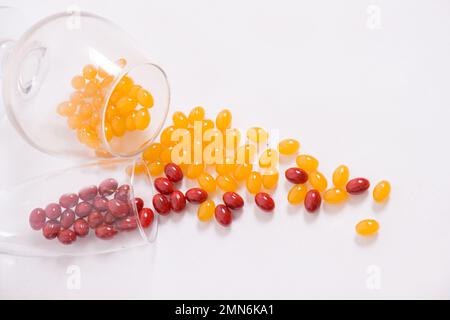 Tabletten, Kapseln zum Sehen. Rote und gelbe Vitamine werden aus dem Glas auf den Tisch gegossen. Dioptrien, Myopie, Weitsicht. Gesunder Körper, Herz und Knochen. Hochwertiges Foto Stockfoto