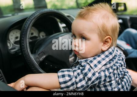 Papa zeigt seinem kleinen Sohn, wie er das Auto fährt, während er hinter dem Steuer sitzt Stockfoto