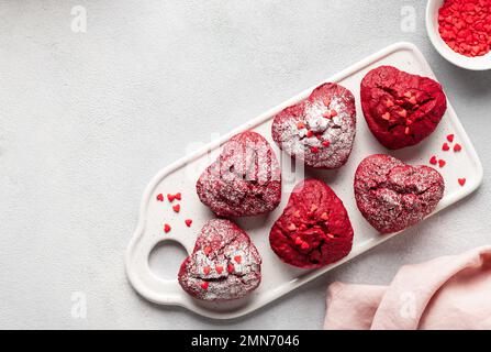 Köstliche herzförmige rote Samt-Cupcakes mit Streuseln auf einem Keramikbrett Stockfoto