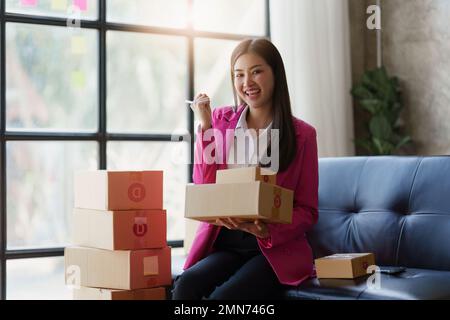 Schöne junge asiatische KMU-Frau, die zu Hause mit einer Kiste arbeitet. Unternehmer kleiner Unternehmen KMU und Lieferkonzept Stockfoto