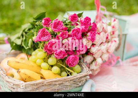 Ein Haufen Früchte und Blumen in einem Korb. Sommerpicknick am Strand an der Küste. Romantisches Partykonzept. Obstkorb. Anwesend. Hochwertiges Obst. Geschenk Stockfoto