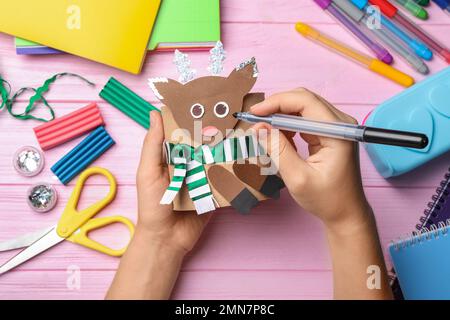 Frau, die Spielzeughirsche aus Toilettenpapier am pinkfarbenen Holztisch macht, Draufsicht Stockfoto