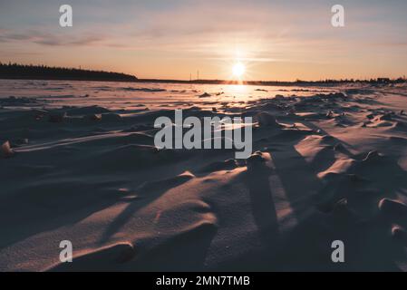 Die Wintersonne geht über dem Wald unter und wirft Schatten von Eisschollen auf den Fluss Vilyui in Yakutia. Stockfoto