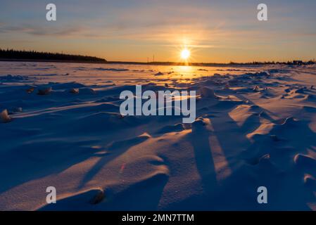 Die helle Wintersonne geht über dem Wald unter und wirft Schatten von den Eisschollen auf dem Fluss Vilyui in Yakutia. Stockfoto