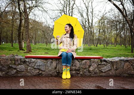 Umgang mit Stress und Angst. Achtsamkeit und Entspannungstechniken üben. Glückliche Seniorin in gelbem Regenmantel mit gelbem Regenschirm Stockfoto