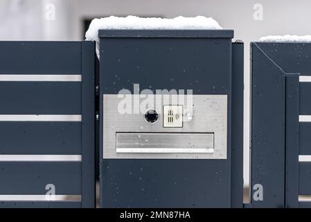 Ein modernes Videotelefon mit einem Briefkasten und einem drahtlosen Kartenleser, montiert in einem Anthrazit-Zaun, sichtbares Wicket, es regnet im Winter. Stockfoto