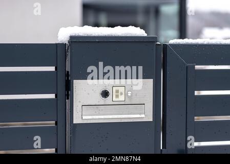 Ein modernes Videotelefon mit einem Briefkasten und einem drahtlosen Kartenleser, montiert in einem Anthrazit-Zaun, sichtbares Wicket, es regnet im Winter. Stockfoto