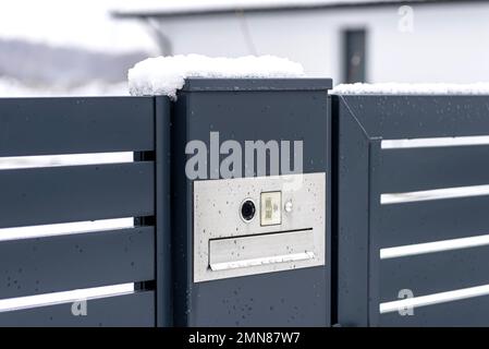 Ein modernes Videotelefon mit einem Briefkasten und einem drahtlosen Kartenleser, montiert in einem Anthrazit-Zaun, sichtbares Wicket, es regnet im Winter. Stockfoto