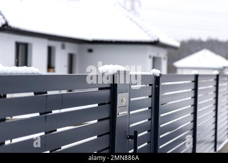 Ein modernes Videotelefon mit einem Briefkasten und einem drahtlosen Kartenleser, montiert in einem Anthrazit-Zaun, sichtbares Wicket, es regnet im Winter. Stockfoto